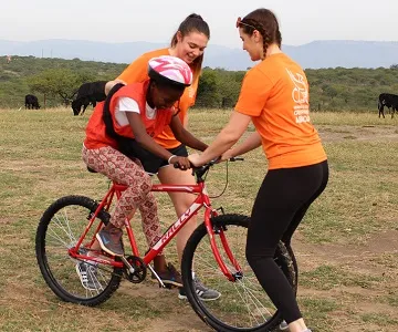 two students helping child ride bike