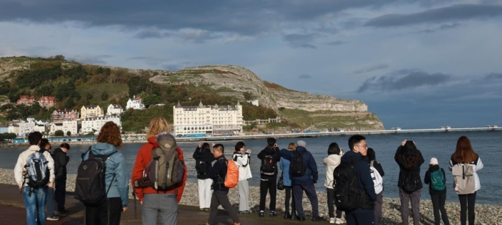 Photo of people on a walk in Llanduno with a view of The Great Orme in the background.