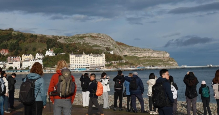 Photo of people on a walk in Llanduno with a view of The Great Orme in the background.