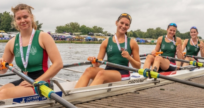 Four female rowers sitting in boat with medals
