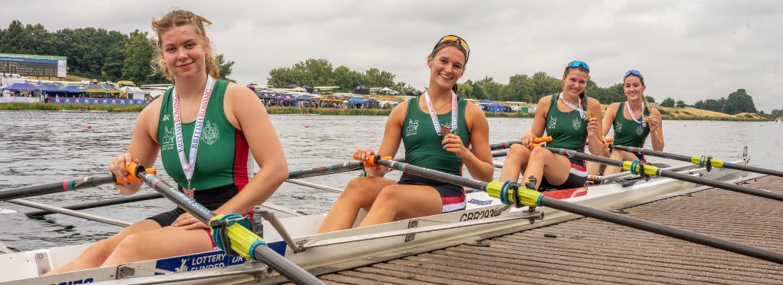 Four female rowers sitting in boat with medals